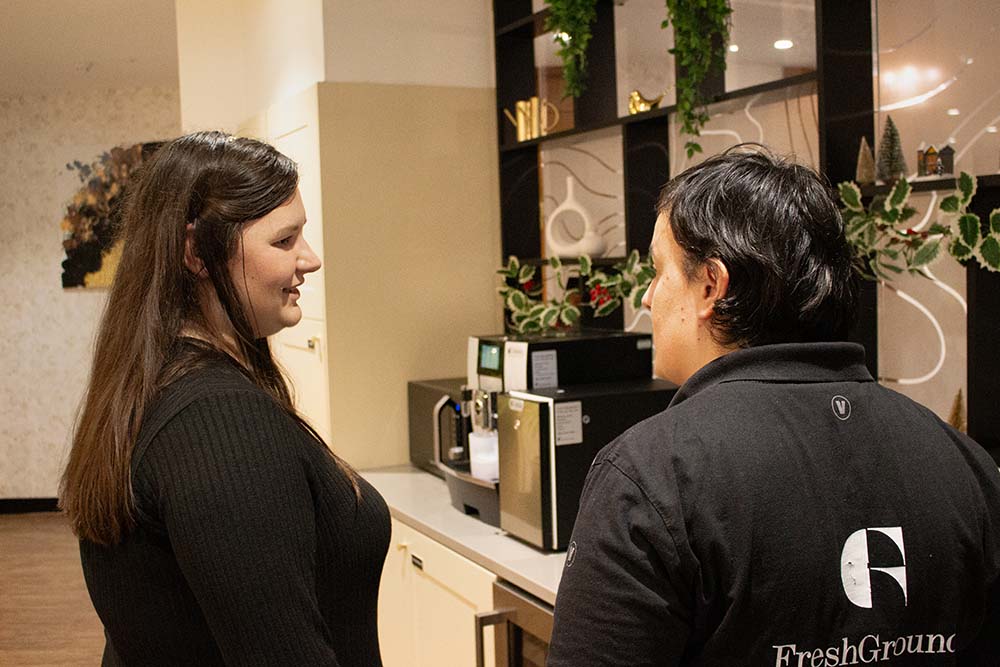 Two people talking over a coffee machine