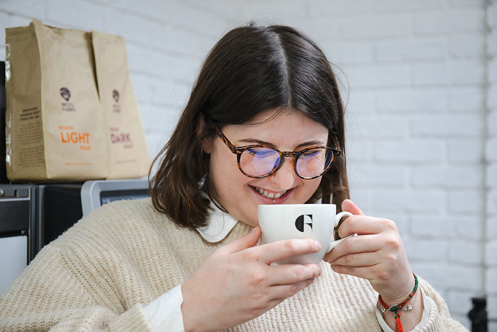 Woman with brown hair laughing into a cup of coffee with the FreshGround logo on it.