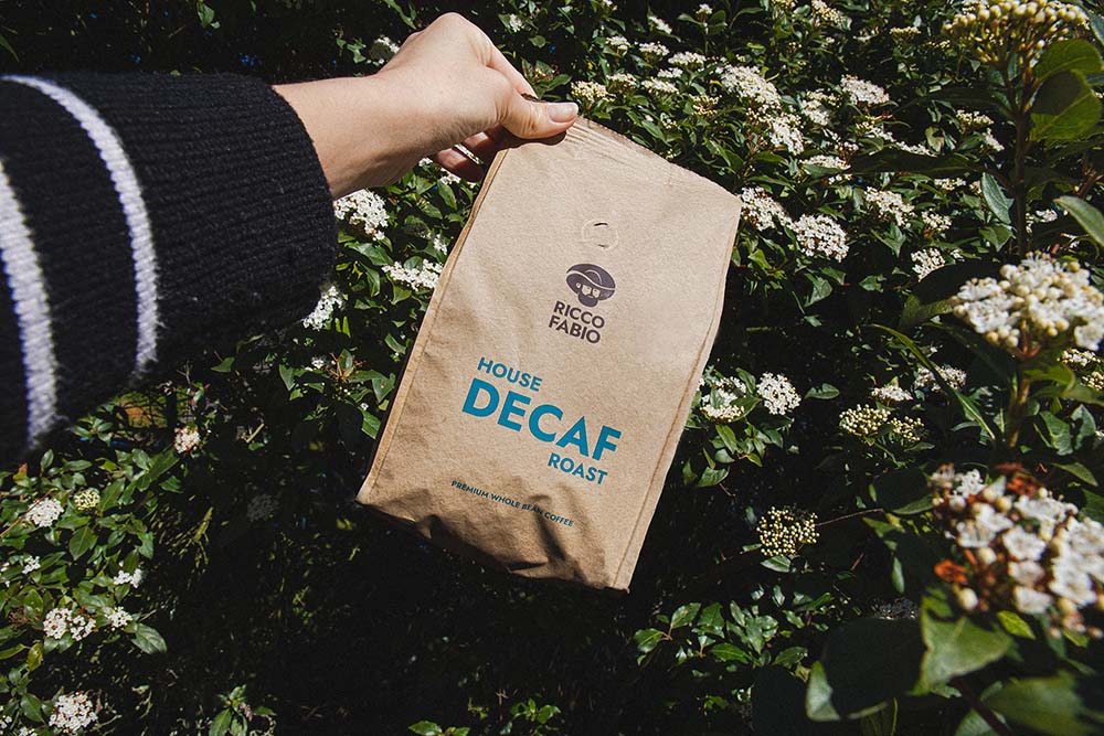 Decaf coffee beans in front of a bush covered in flowers